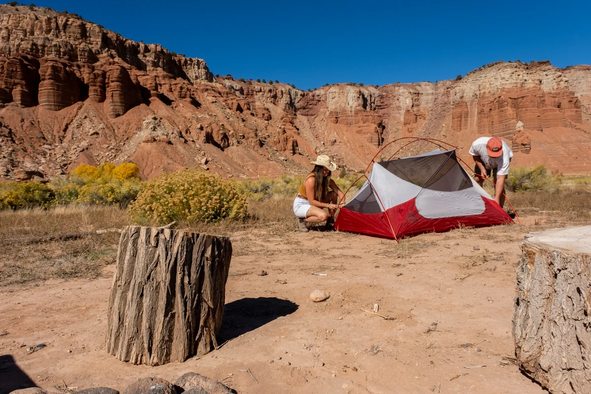 Camper packing a sleeping bag into a stuff sack beside camping gear