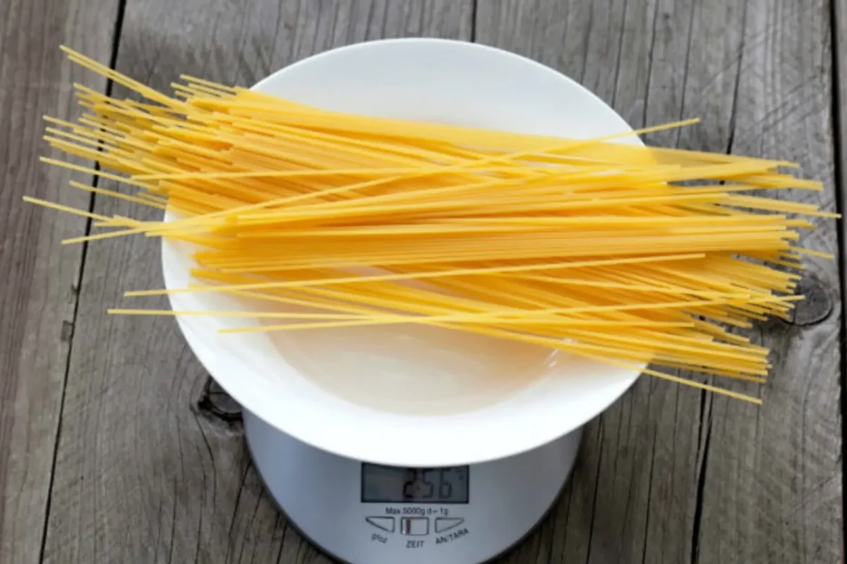 Dry pasta measuring cup next to cooked spaghetti and penne on a kitchen counter